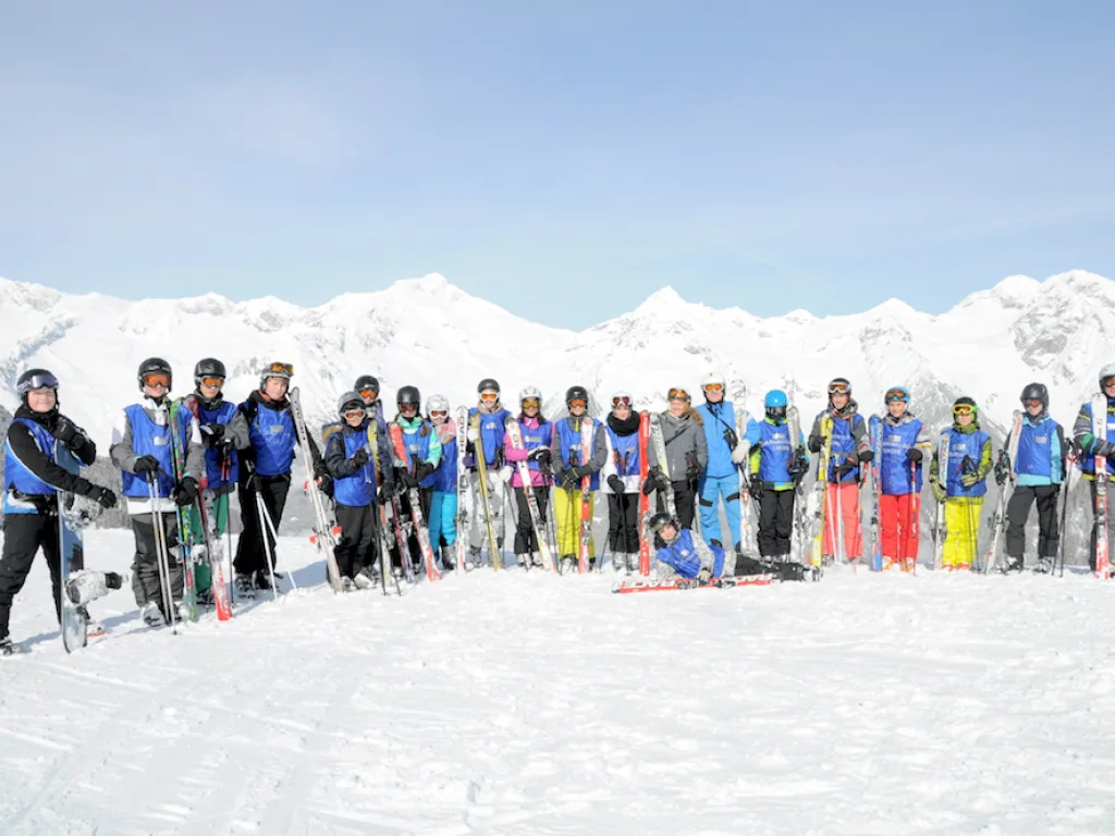Lange Reihe von Jugendlichen auf der Piste vor Bergpanorama.